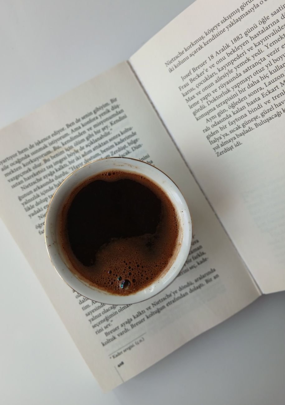 Top view of a cup of dark coffee placed on an open book, creating a cozy reading scene.
